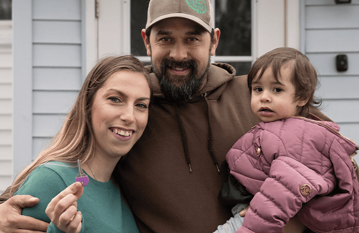 Family holding a key in front of their home